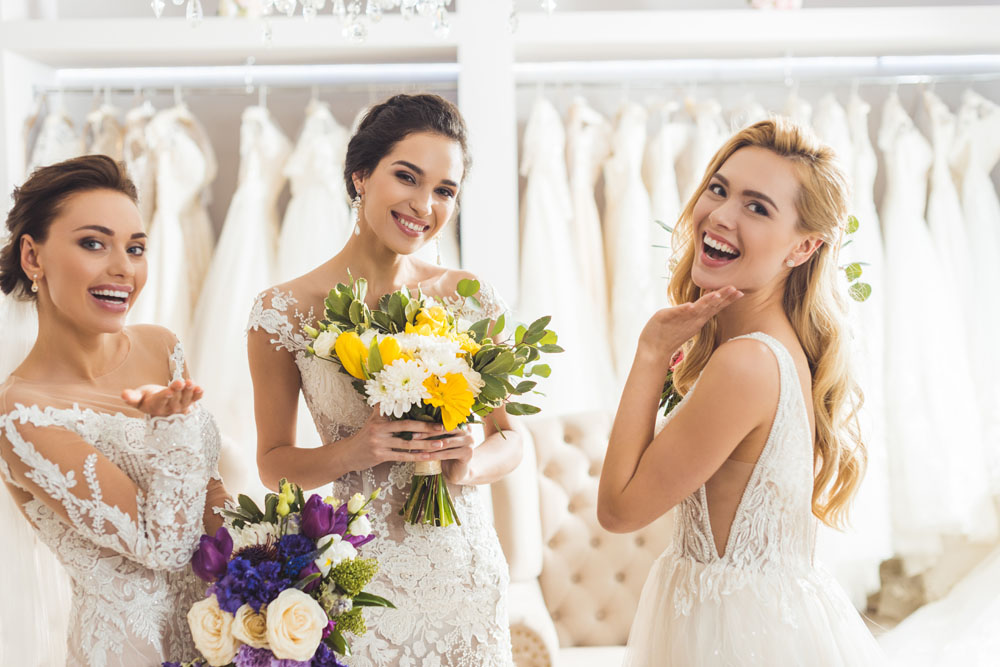 Smiling women in wedding dresses with flowers in wedding salon